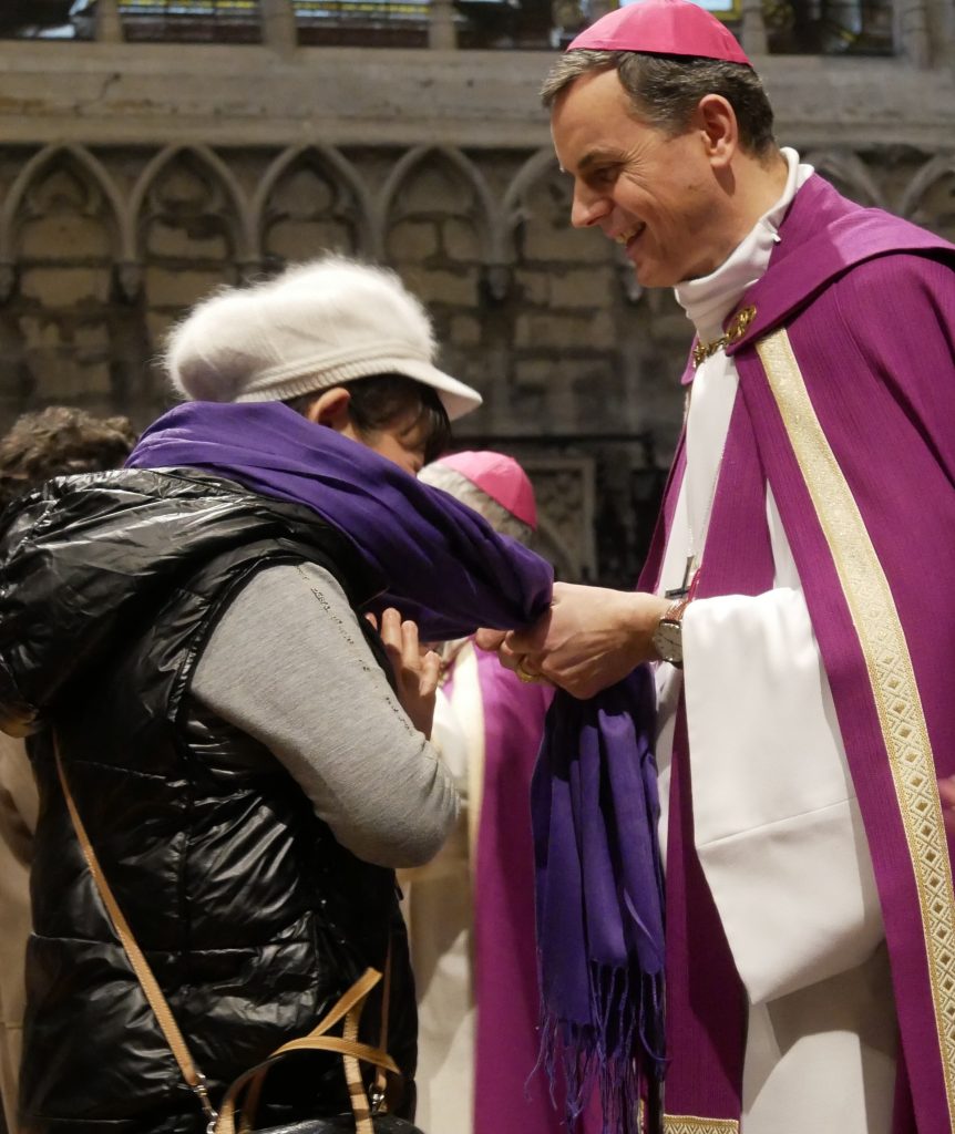 Photo de Mgr Luc Terlinden remettant une écharpe violette à une catéchumène lors de l'appel décisif