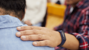 Photo d'un accompagnement spirituel. On voit la main d'une personne sur l'épaule d'une autre en signe de soutien bienveillant.